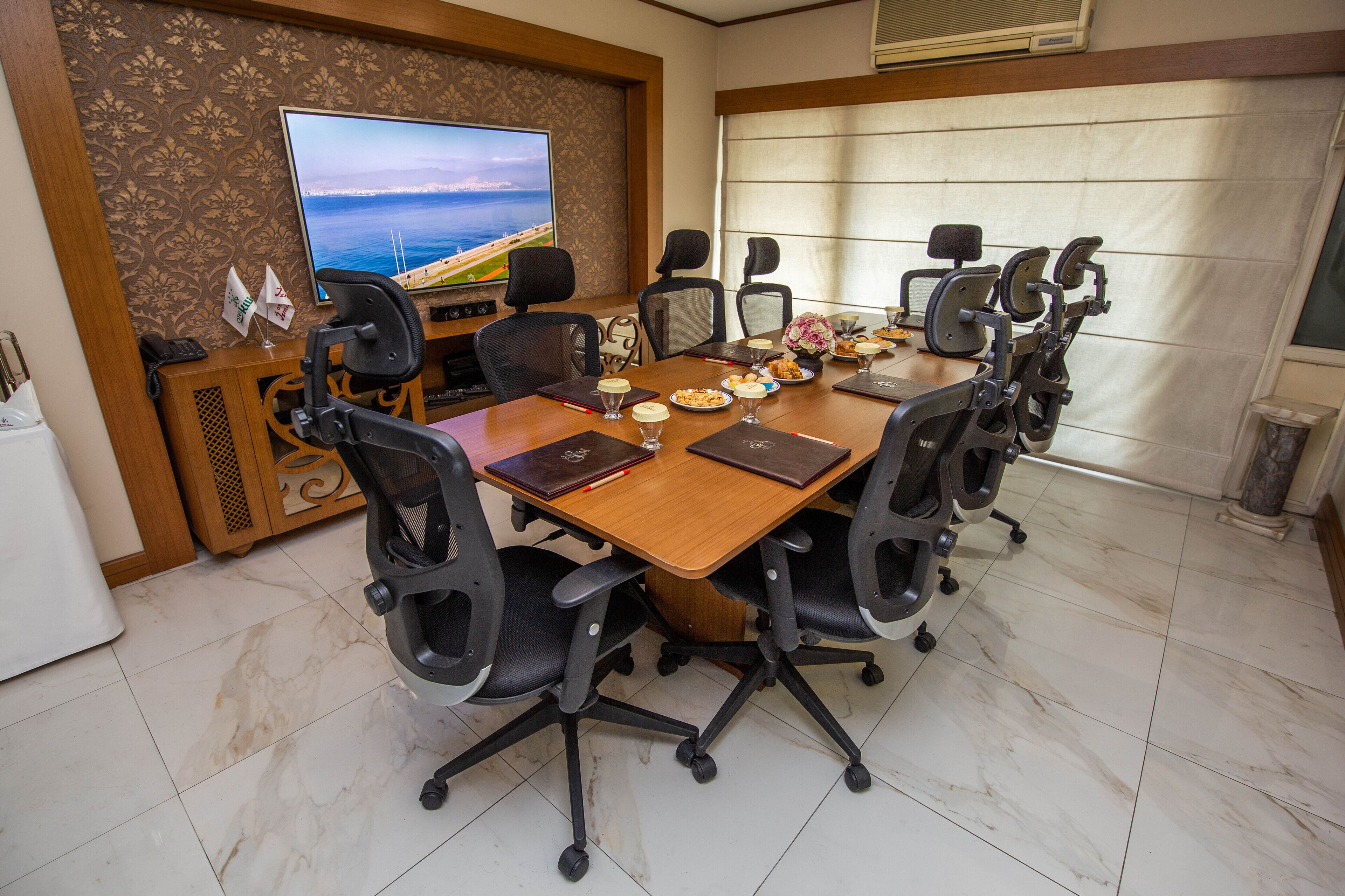 Un salón de conferencias con una mesa grande, varias sillas, una televisión y una decoración en la pared.