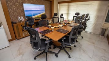Un salón de conferencias con una mesa grande, varias sillas, una televisión y una decoración en la pared.