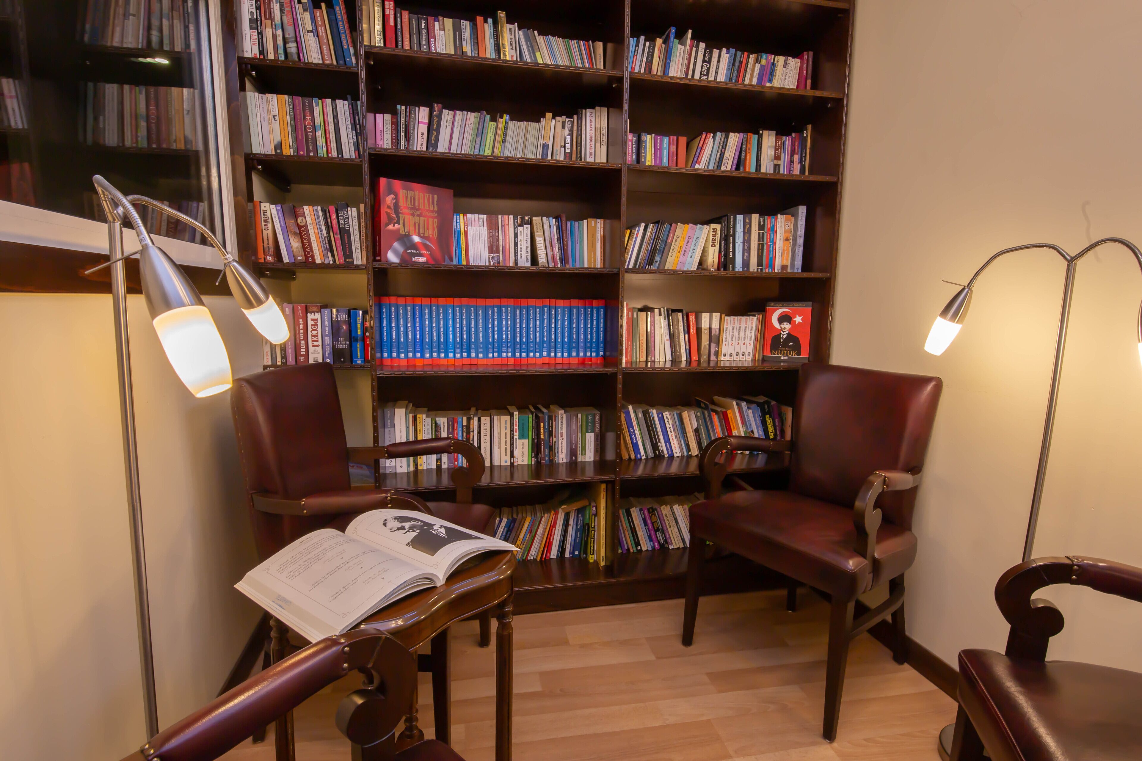 Una biblioteca con estanterías, sillones de cuero y dos lámparas de pie.