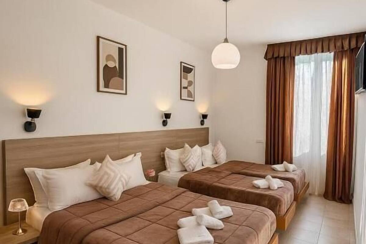 A hotel room with two beds, a nightstand, a lamp, and a ceiling light.