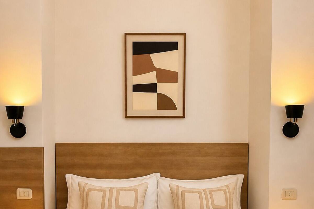 A hotel room with a large bed, two bedside lamps, a framed abstract artwork, and a folded towel on the bed.