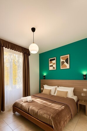 Un dormitorio con una cama, cortinas, una lámpara de pared y dos cuadros enmarcados.