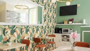 Un comedor con un muro de diseño geométrico, un televisor de pantalla plana y una cocina equipada.
