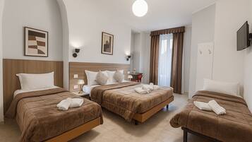 A hotel room with three beds, a TV, a lamp, and a window with curtains.