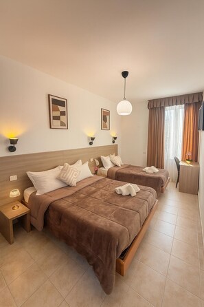 Habitación de hotel con dos camas, un escritorio, una silla y un ventanal con cortinas.