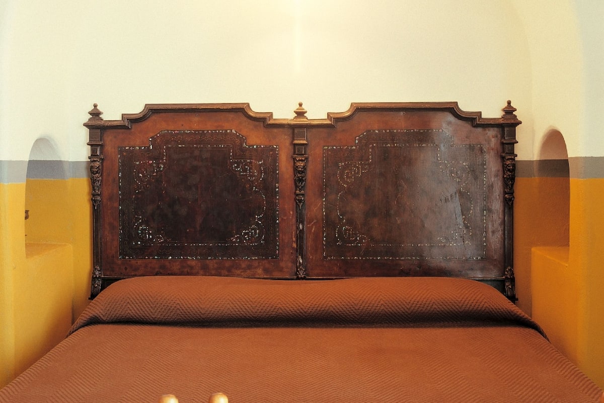 A bed with a wooden headboard, a brown bedspread, and two side tables with a patterned design.