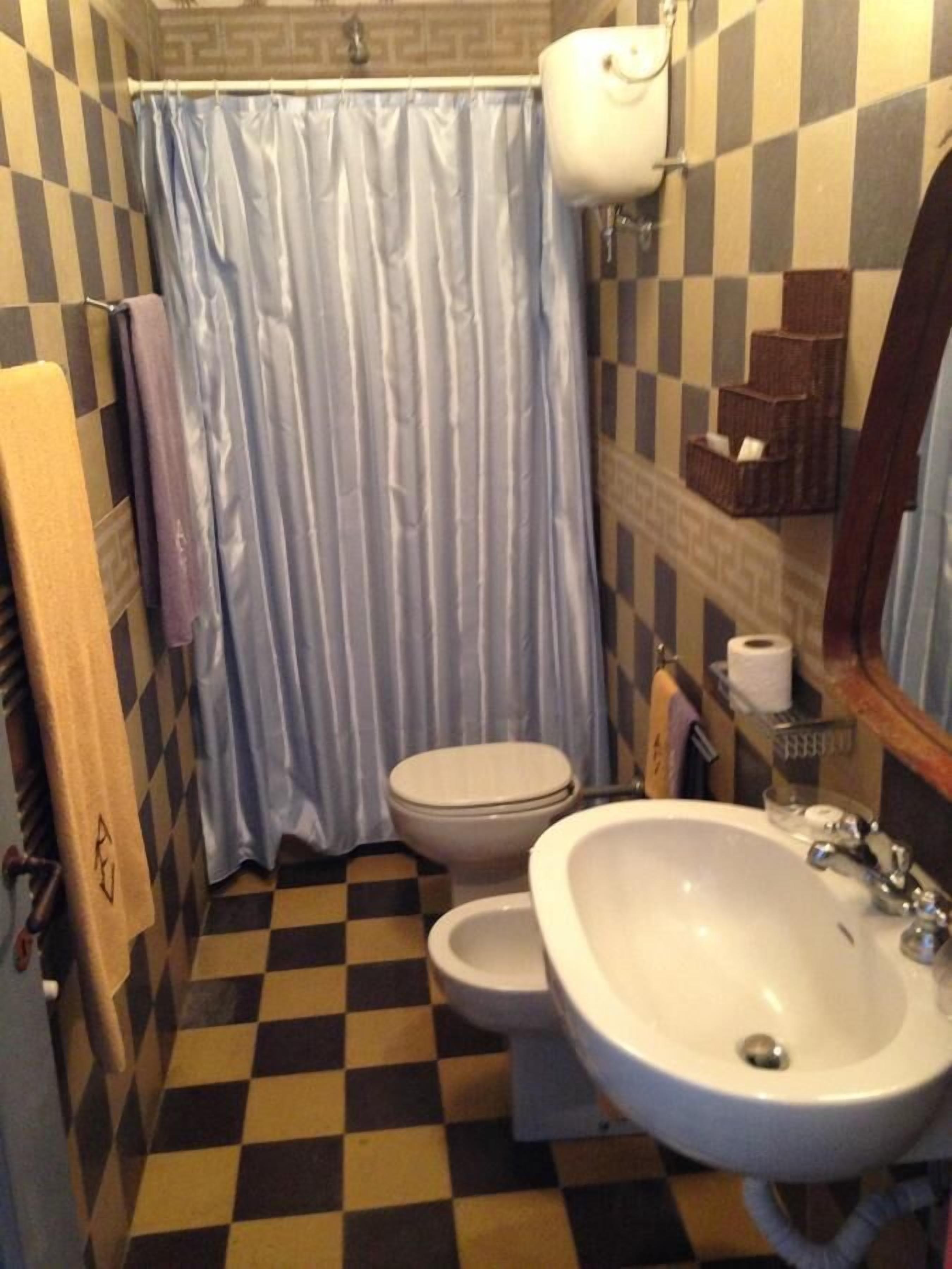 A bathroom with a checkered floor, a white sink, a toilet, and a blue shower curtain.