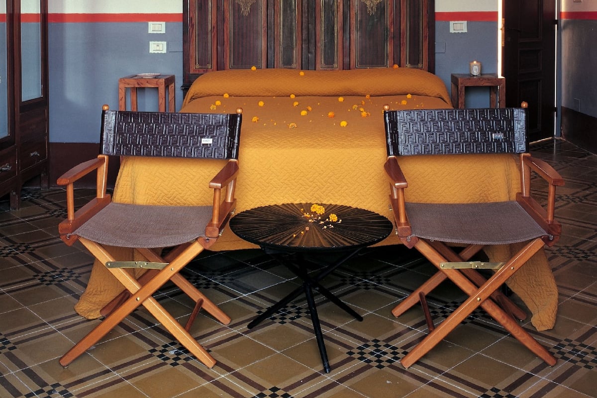 A hotel room with a large bed, two armchairs, a small table, and a decorative wall with framed artwork.
