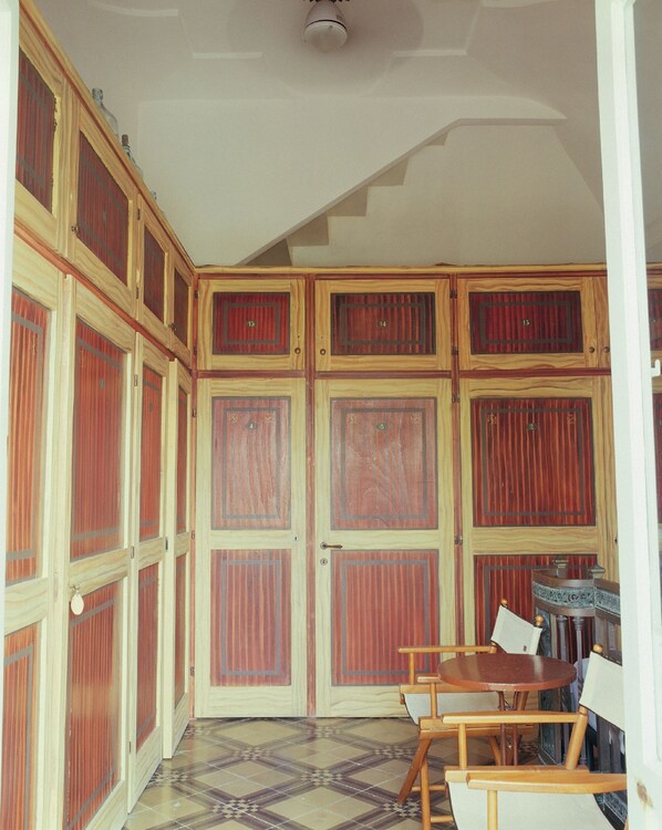 A room with a checkered floor, wooden cabinets with numbered doors, a table with chairs, and a ceiling light fixture. - Villa Laetitia (Ponza)