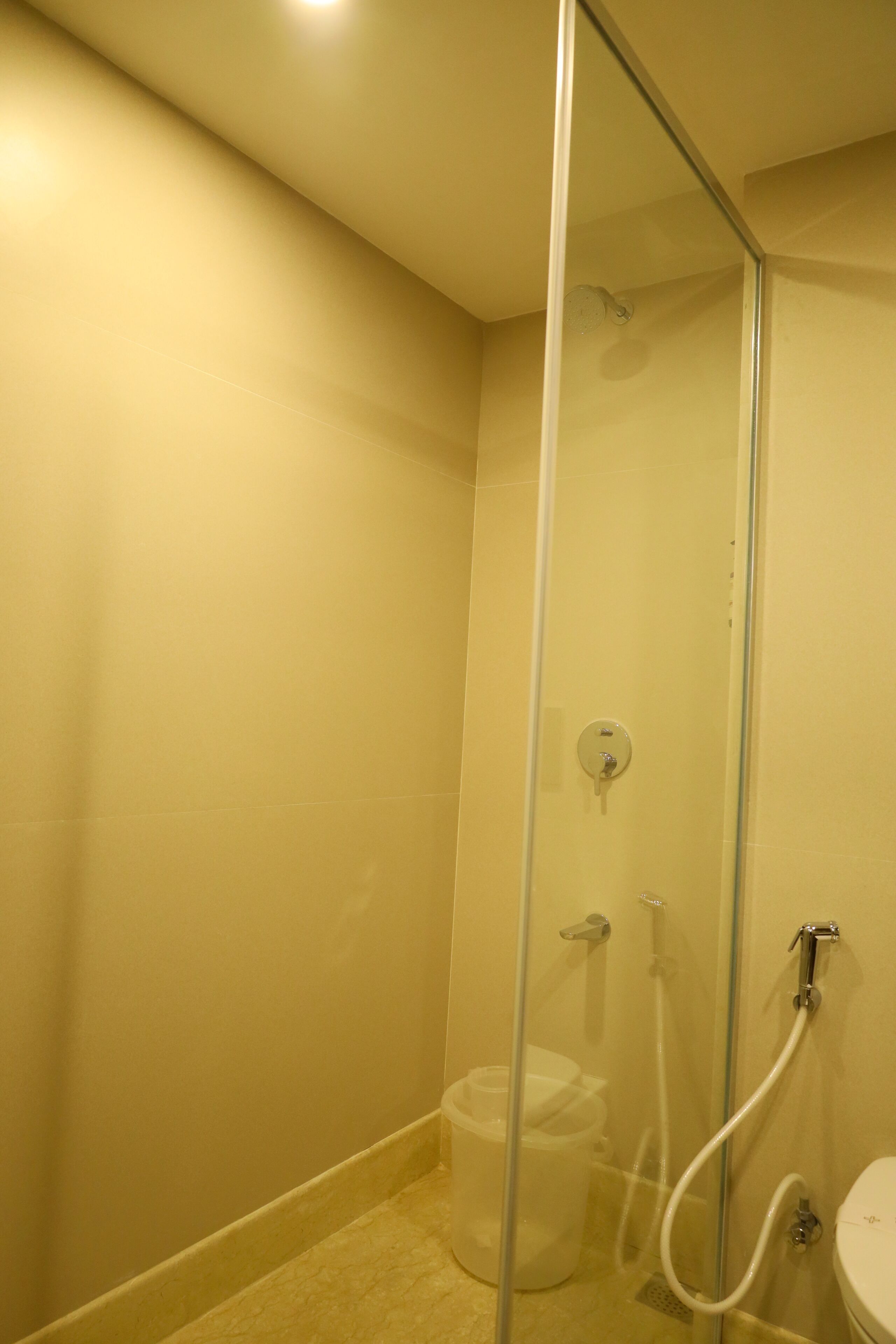 A bathroom with a glass shower enclosure, a toilet, and a trash bin.