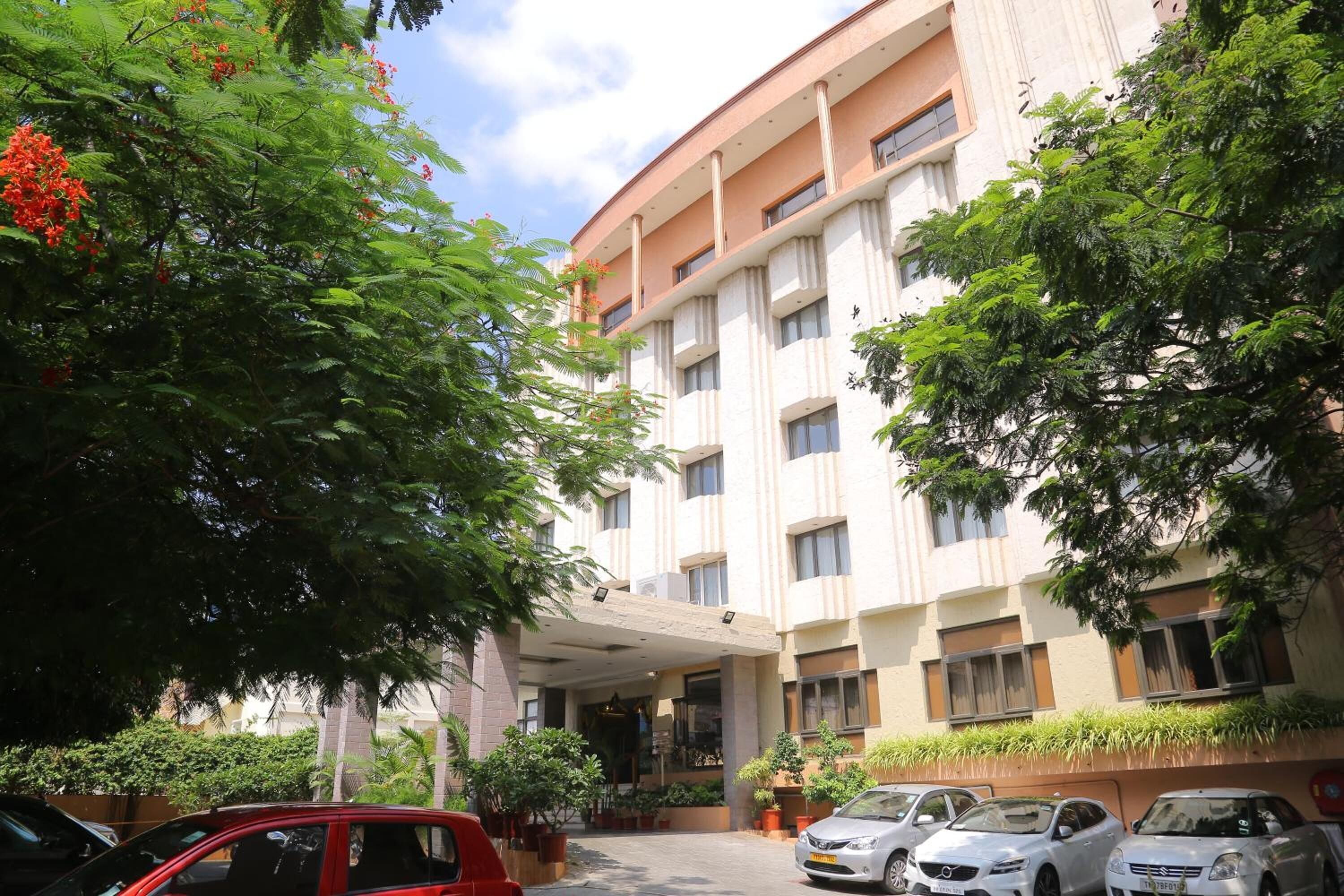 A multi-story hotel with a central entrance, surrounded by lush greenery and parked cars.