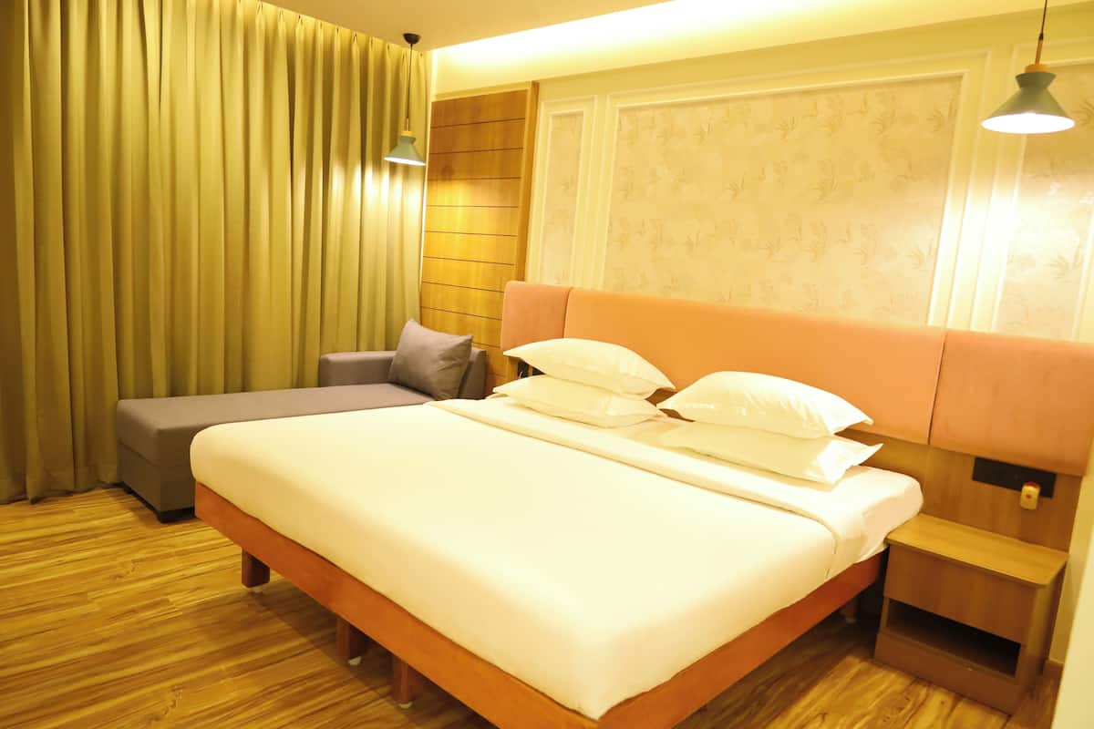 A hotel room with a large bed, a bedside table, a nightstand, a sofa, and a curtain.