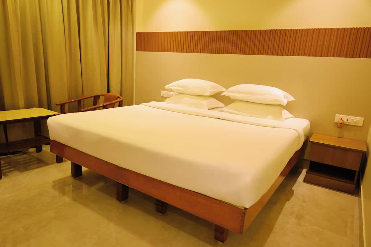 A hotel room with a large bed, a wooden nightstand, a bedside table, and a chair.