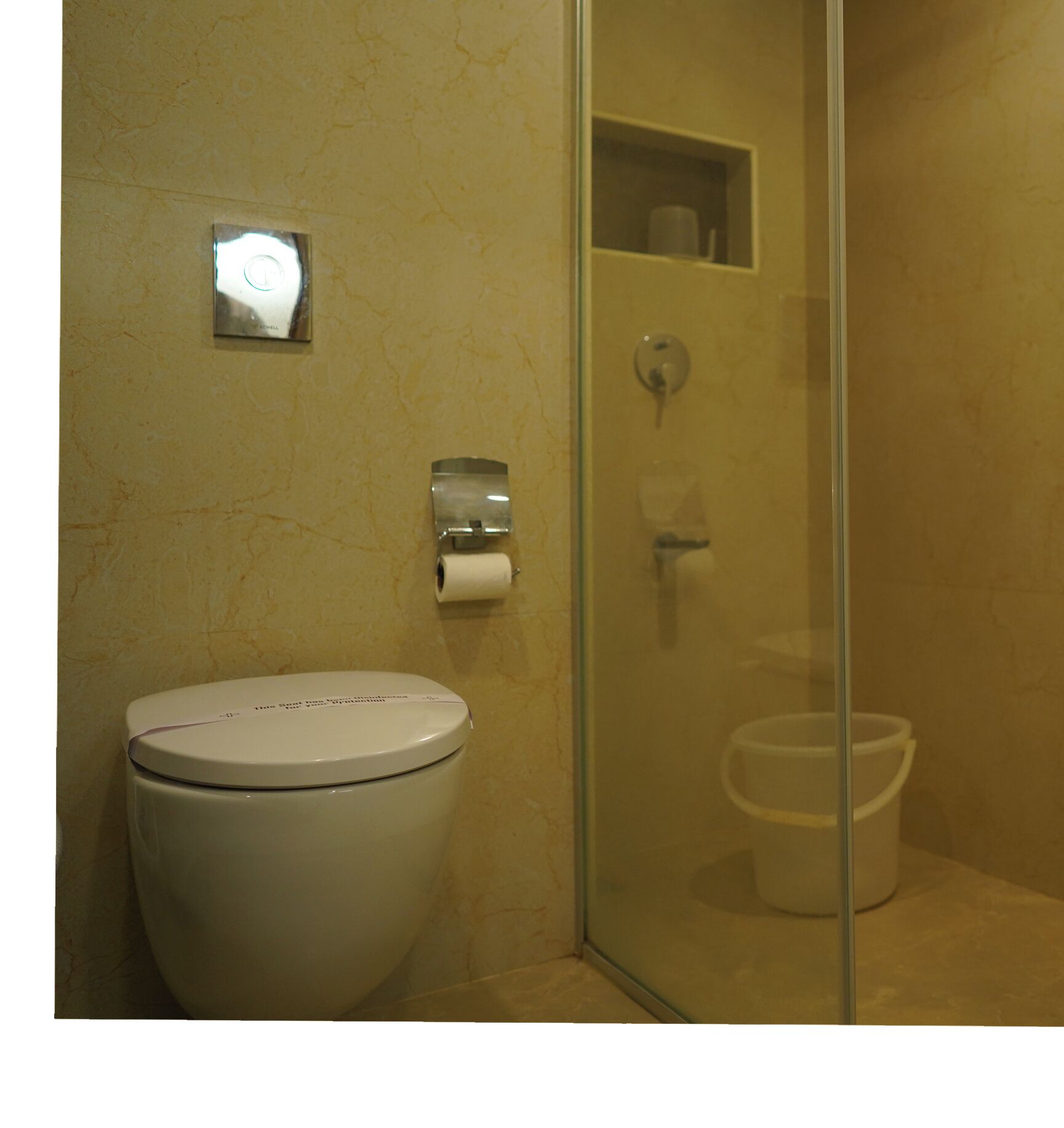A bathroom with a toilet, a paper towel dispenser, and a glass shower enclosure.