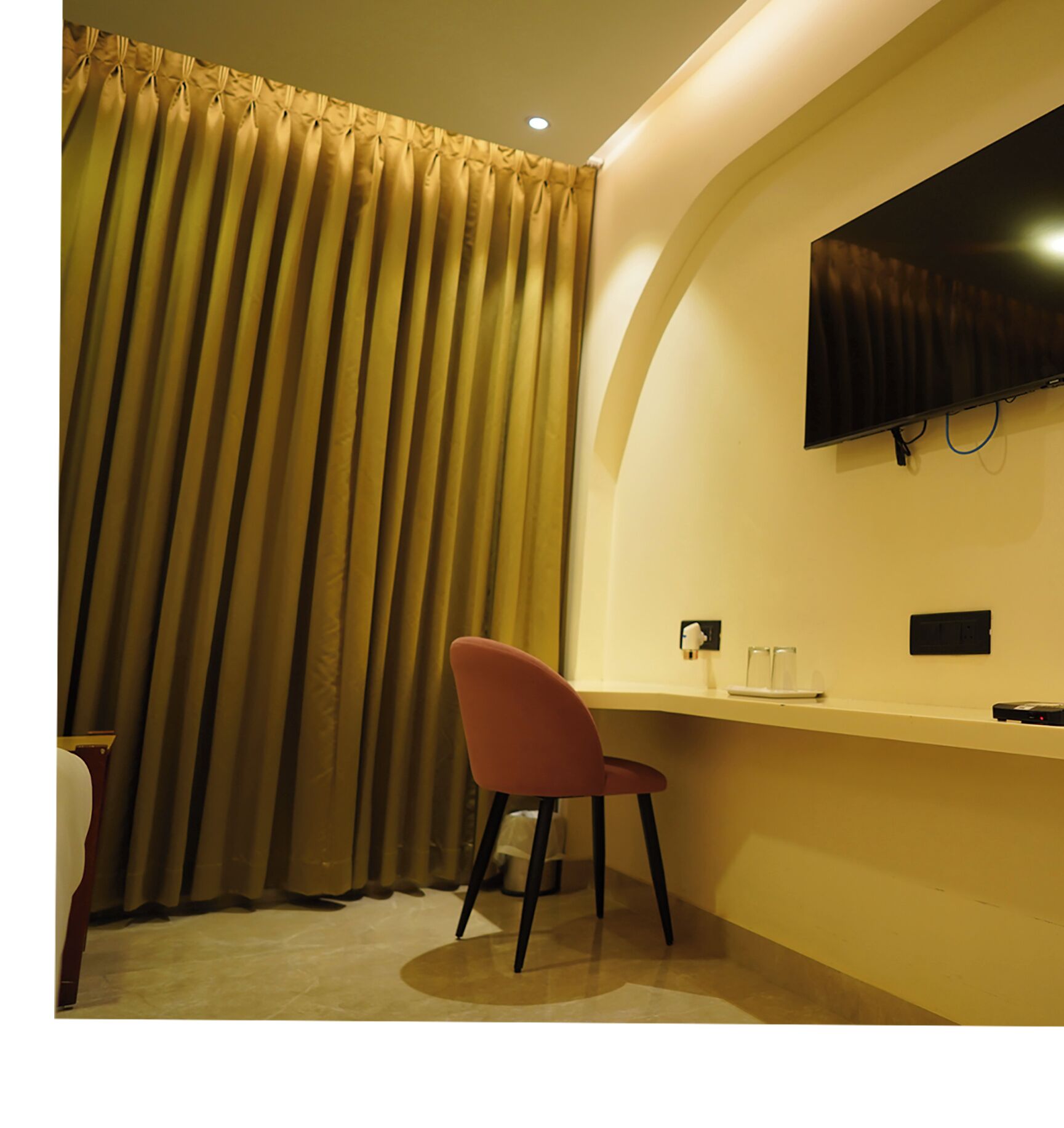 Una habitación con un ventanal grande, un televisor de pantalla plana montado en la pared, un escritorio con una silla y una mesita de noche con una lámpara.