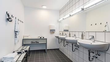 A modern bathroom with three sinks, a bench with towels, and a mirror with lights.
