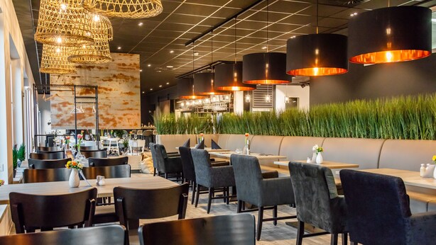 Interior moderno de restaurante con varias mesas y sillas para comer, iluminación decorativa y una pared verde cubierta de plantas.