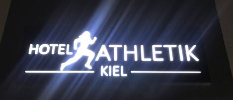 Une enseigne portant l’inscription « HÔTEL ATHLETIK KIEL » et représentant une silhouette en train de courir.