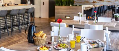 A breakfast setting with a wooden table, white chairs, and a variety of breakfast items including bread, eggs, and juice.