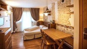 Een kleine kamer met een bed, houten tafel en een stenen muur.