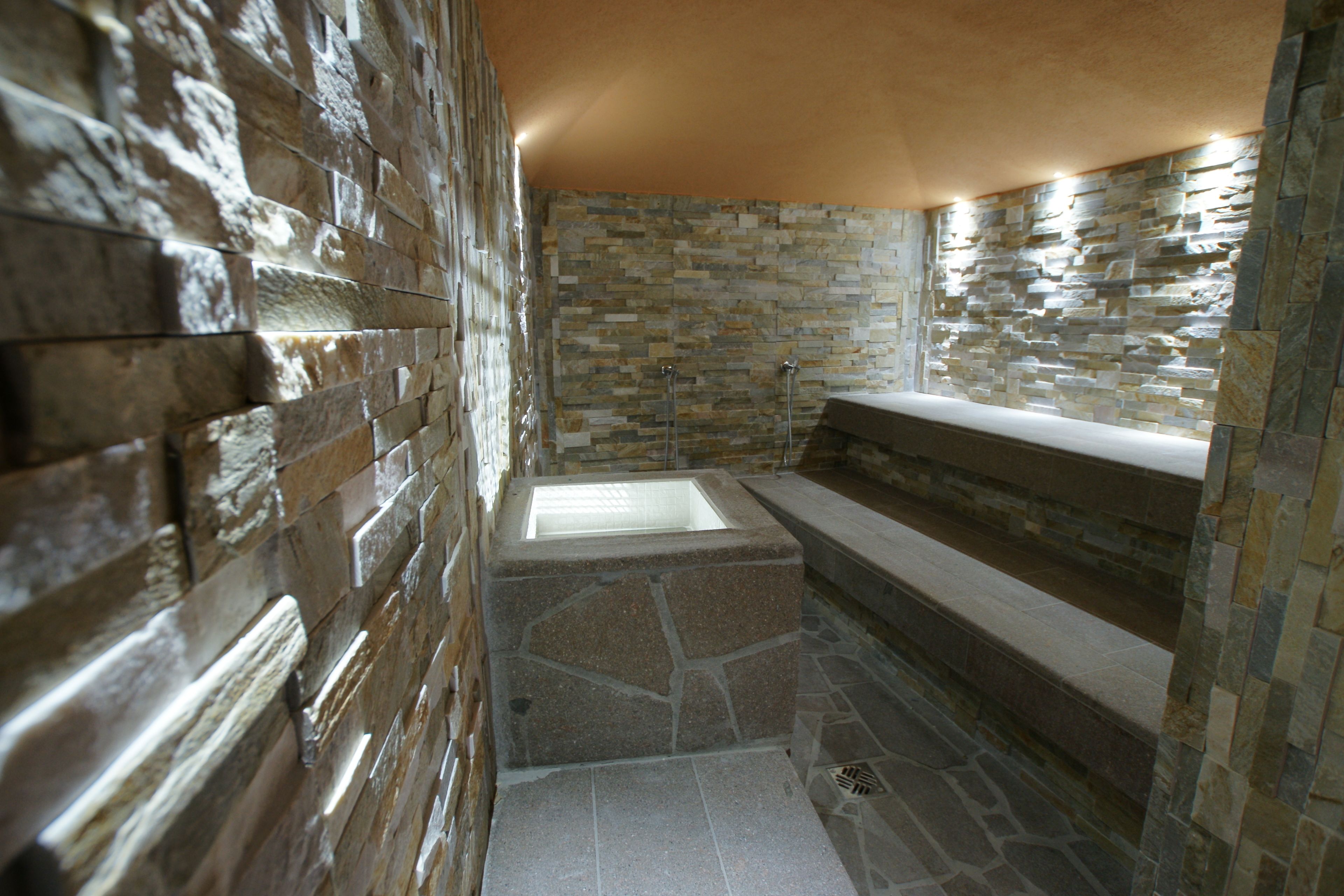 A stone-walled bathroom with a built-in bathtub and a shower area.