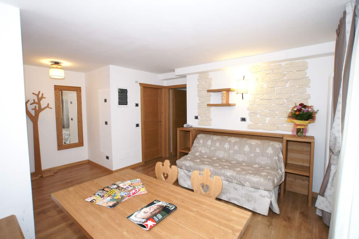 A cozy room with a wooden table, a sofa, a stone wall, and a mirror.