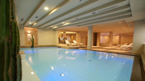 Una piscina interior con agua azul cristalina, rodeada de sillas de descanso y una planta de cactus.