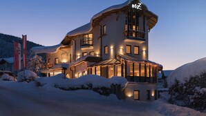 A snow-covered hotel with a prominent 'MZ' sign, multiple balconies, and a well-lit facade. - meiZeit Lodge (Filzmoos)