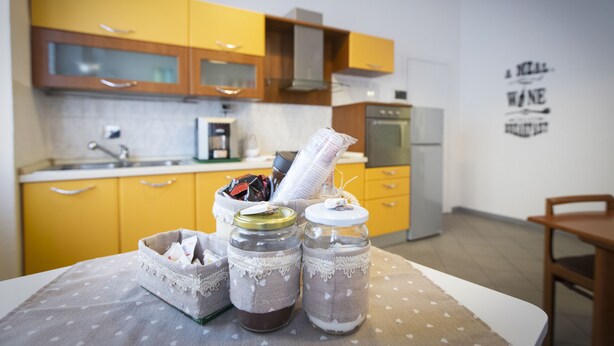 A kitchen with yellow cabinets, a refrigerator, and a table with jars and a basket.