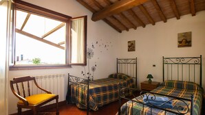 Una habitación con dos camas, una silla de madera, una ventana con vistas y un radiador.