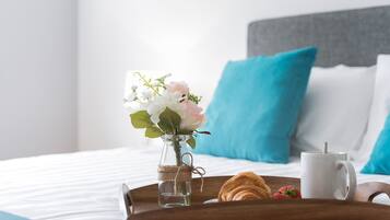 A neatly made bed with a tray containing a croissant, a strawberry, and a white mug. A small vase with flowers is placed on the bed.