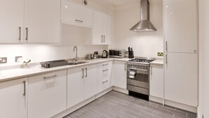 A modern kitchen with white cabinets, stainless steel appliances, and a tiled floor. - KVM - Jubilee Mansions 2 (Peterborough)