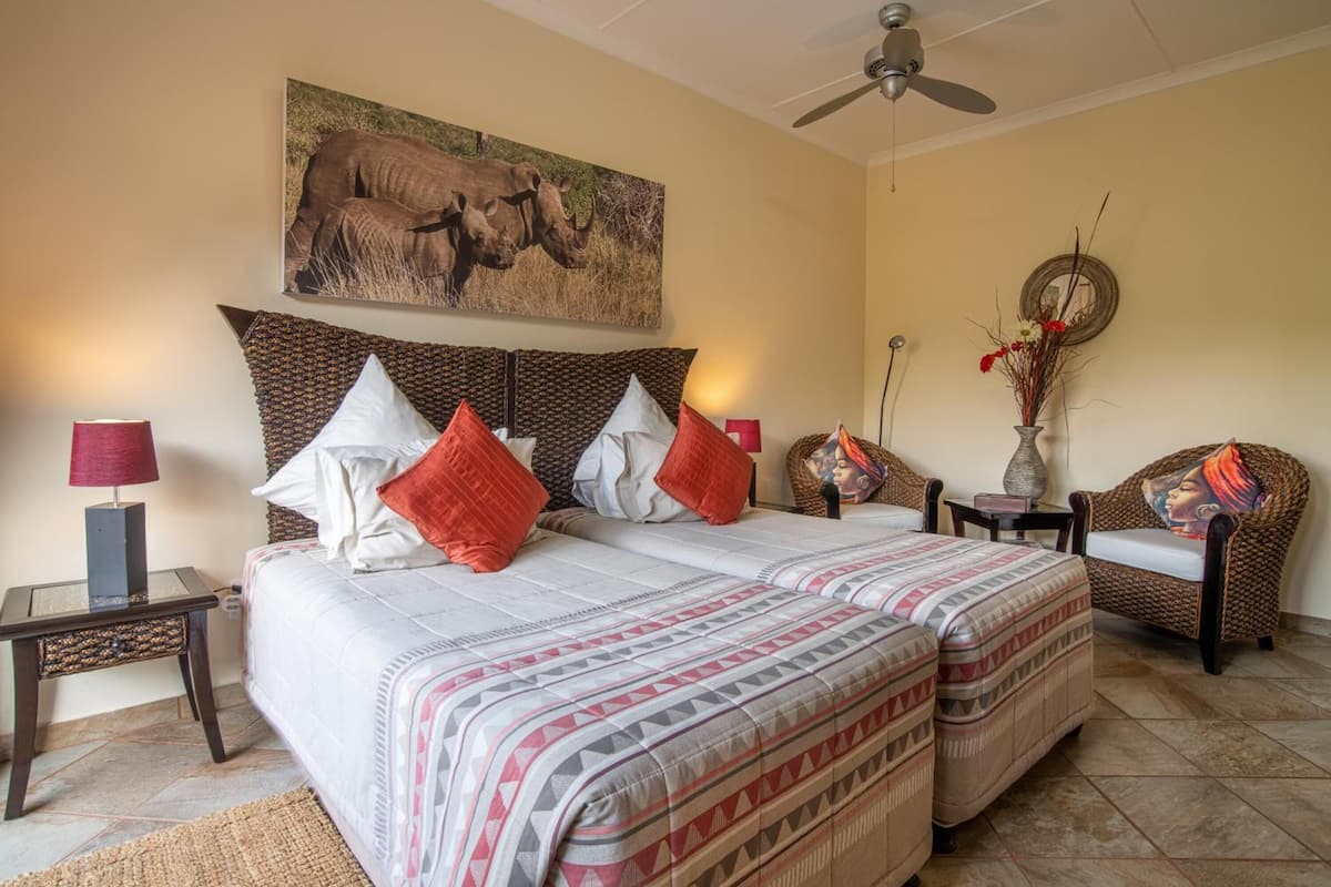 Ein Schlafzimmer mit einem großen Bett, zwei Kissen, einem Nachttisch, einem Sessel, einem Wandbild und einem Deckenventilator.