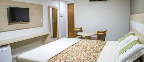 Una habitación de hotel con cama, escritorio, silla, televisor y aire acondicionado.