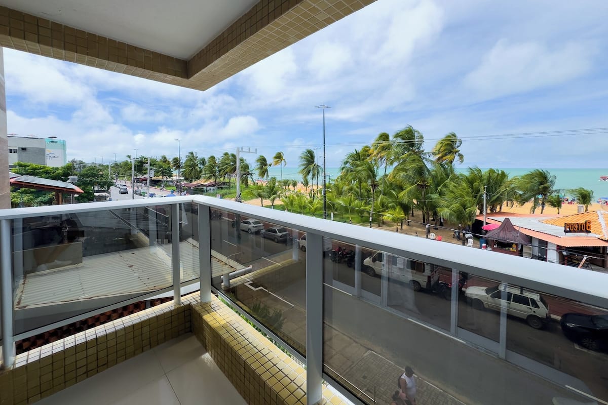 A balcony with a view of a beach, palm trees, and a street with cars.