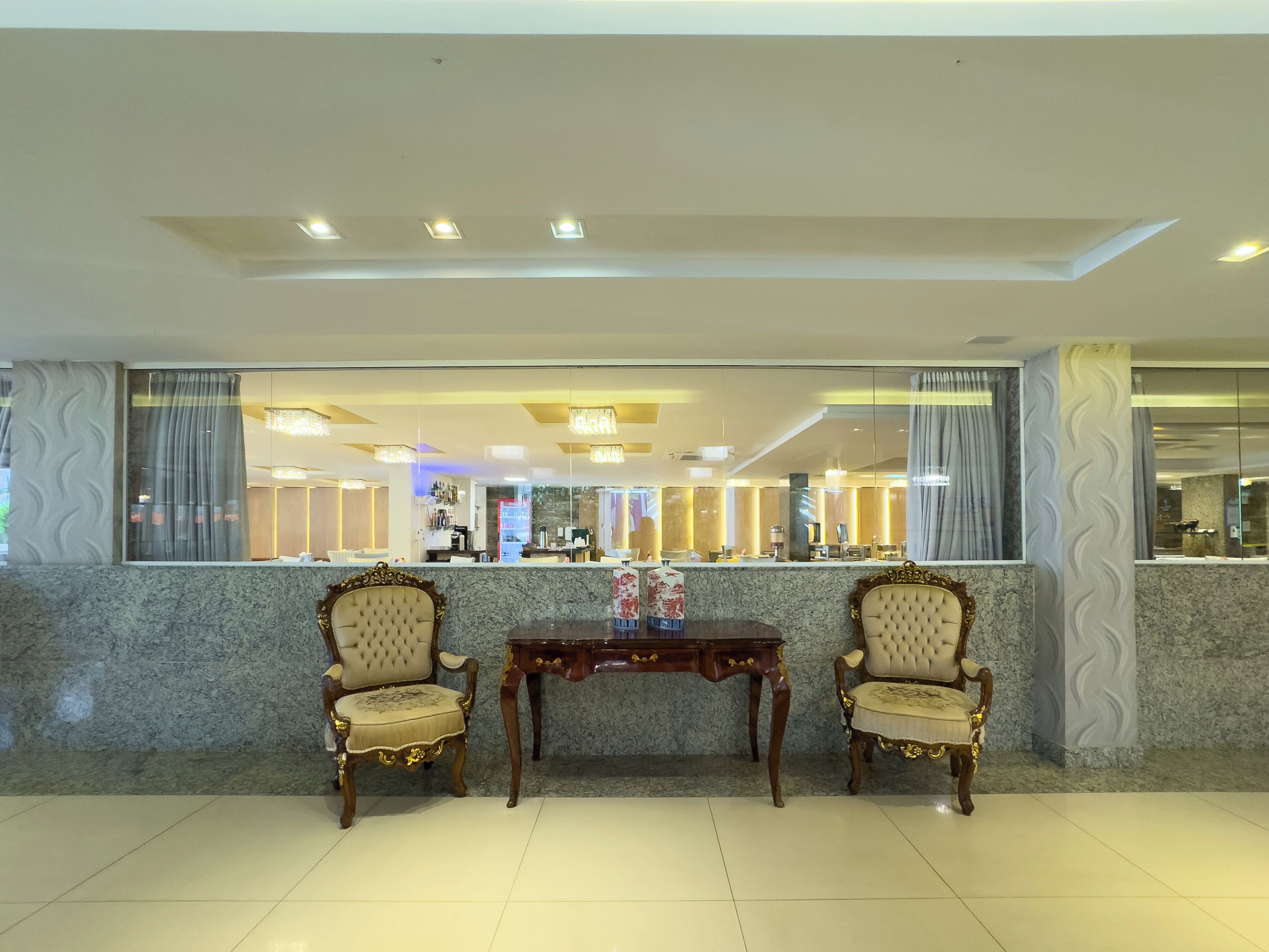 A lobby with two ornate chairs, a marble reception desk, and a modern chandelier.