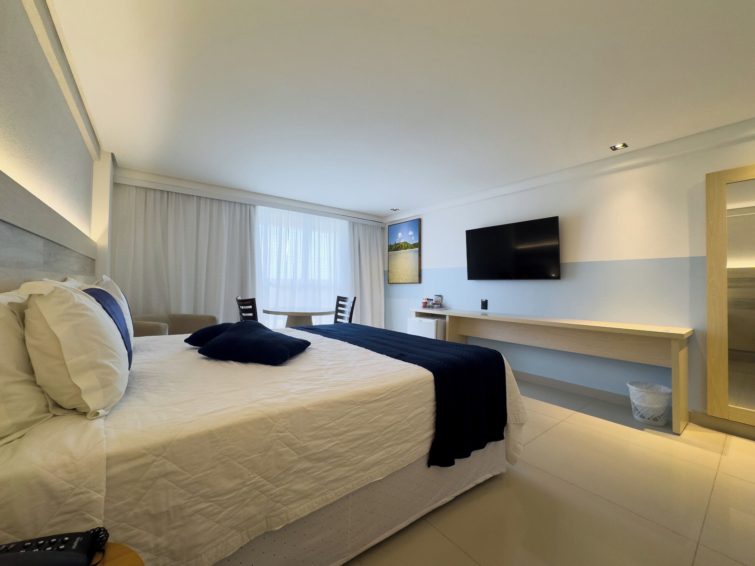 Habitación de hotel con una cama grande, un escritorio, una silla, un televisor y una ventana con cortinas.