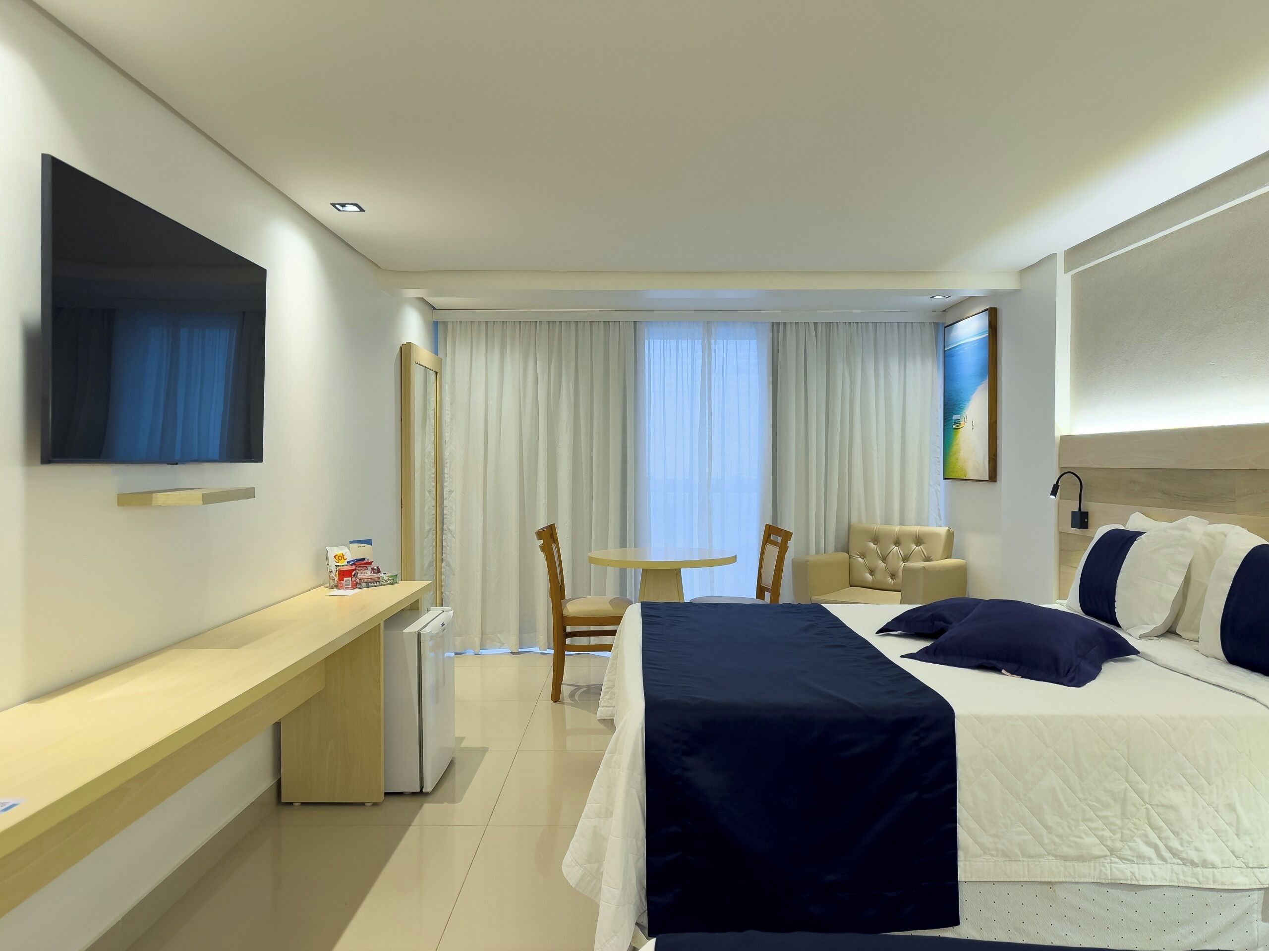 Une chambre d’hôtel avec un lit, un bureau, une chaise, une petite table, une télévision et une fenêtre avec des rideaux.