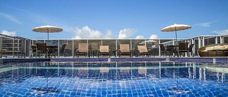 A pool with clear blue water and a tiled edge, surrounded by lounge chairs and umbrellas.