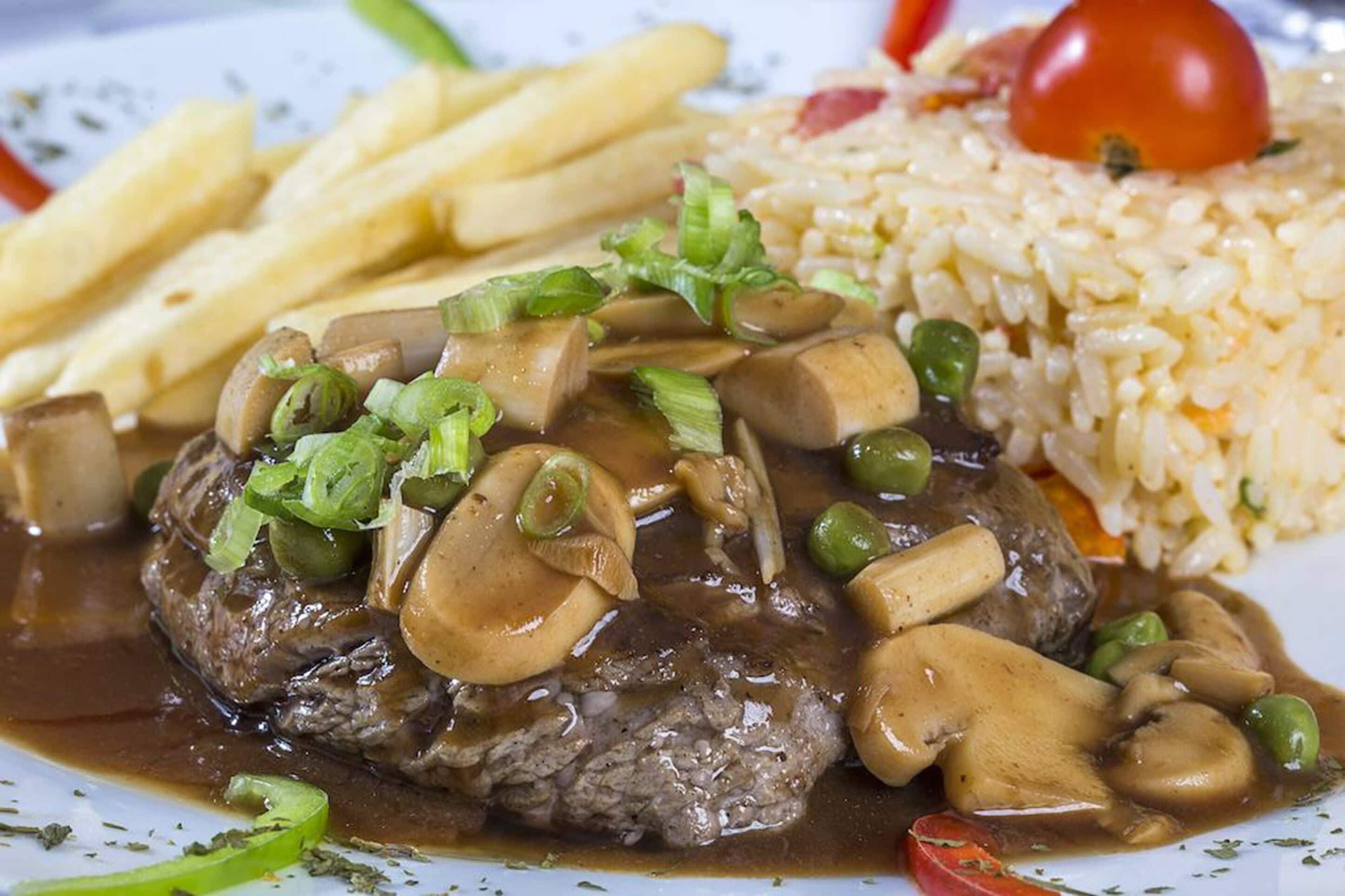 A steak with mushrooms and green onions, served with French fries and rice.