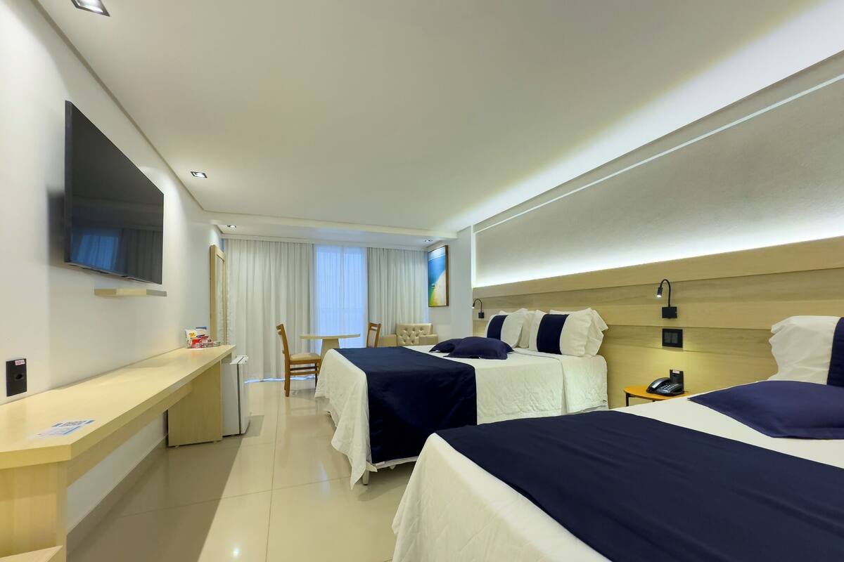 A hotel room with two beds, a desk, a chair, a TV, and a window with curtains.