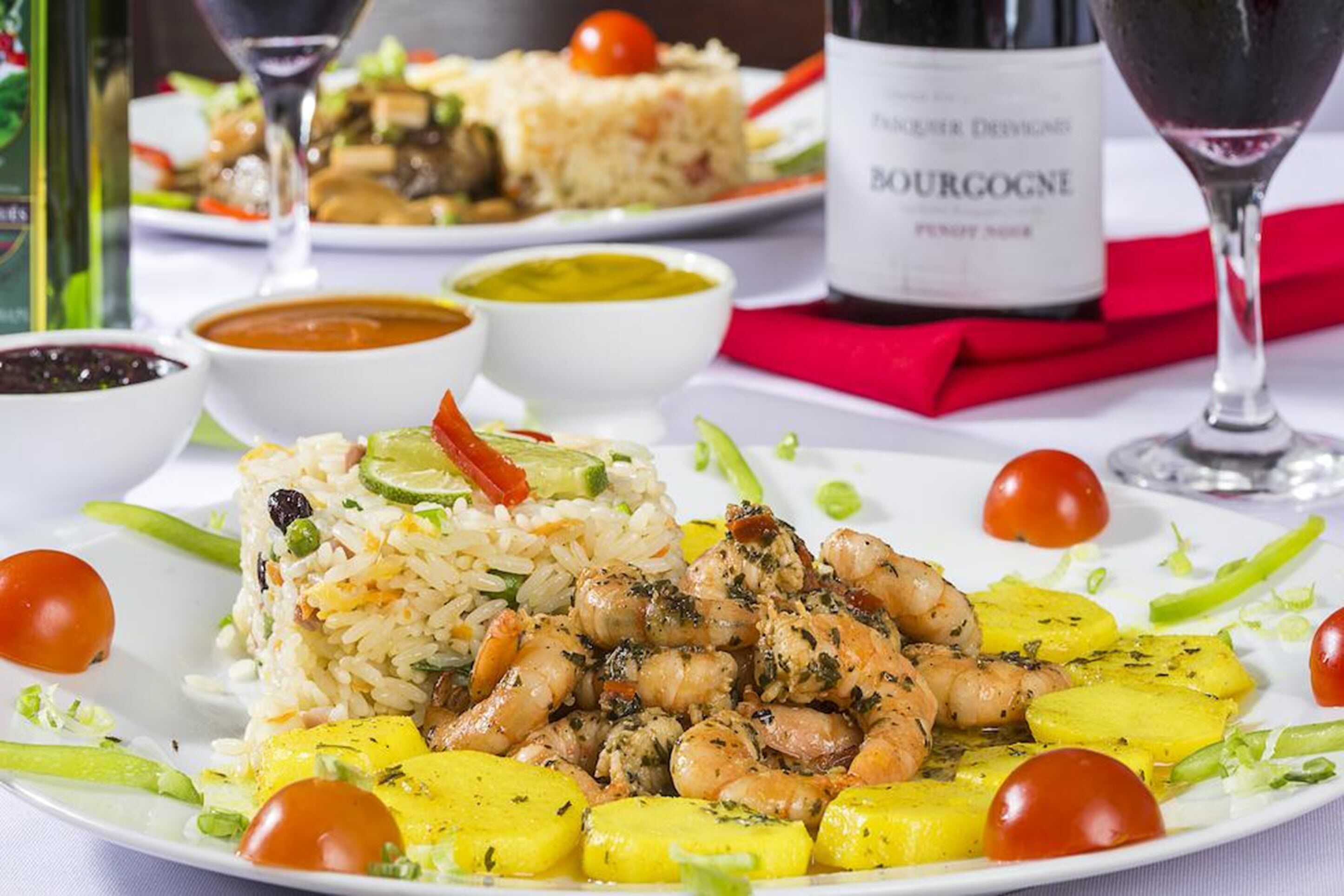 A plate of food with rice, shrimp, and vegetables, accompanied by a bottle of wine and glasses.