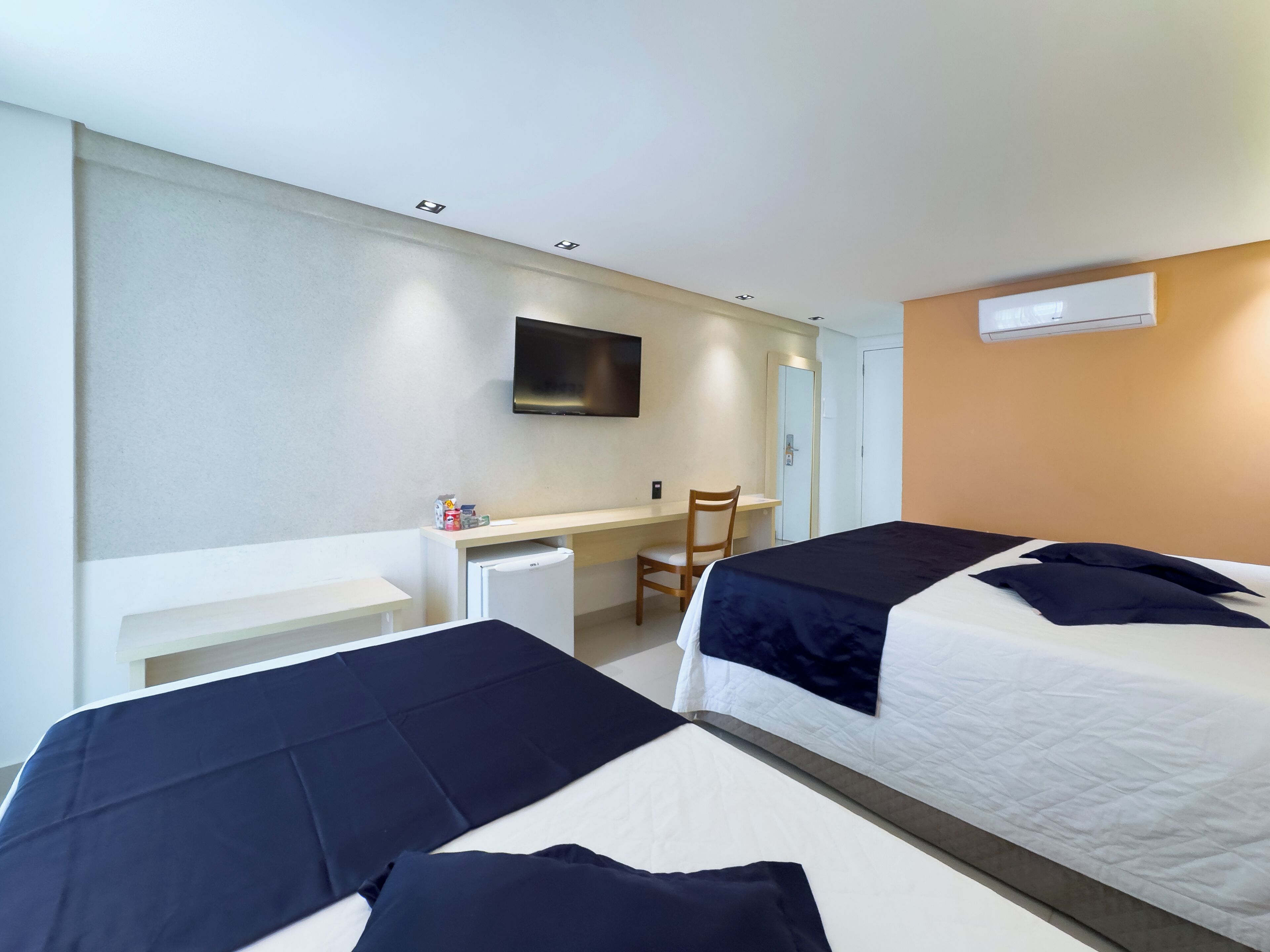 Ein Hotelzimmer mit zwei Betten, einem Schreibtisch, einem Sessel, einem Fernseher und einer Klimaanlage.
