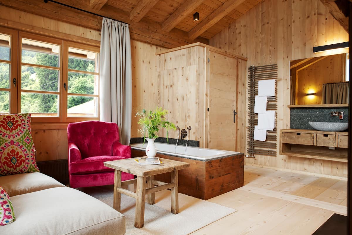 A wooden interior with a red chair, a wooden table, a bathtub, and a sink with a stone basin.
