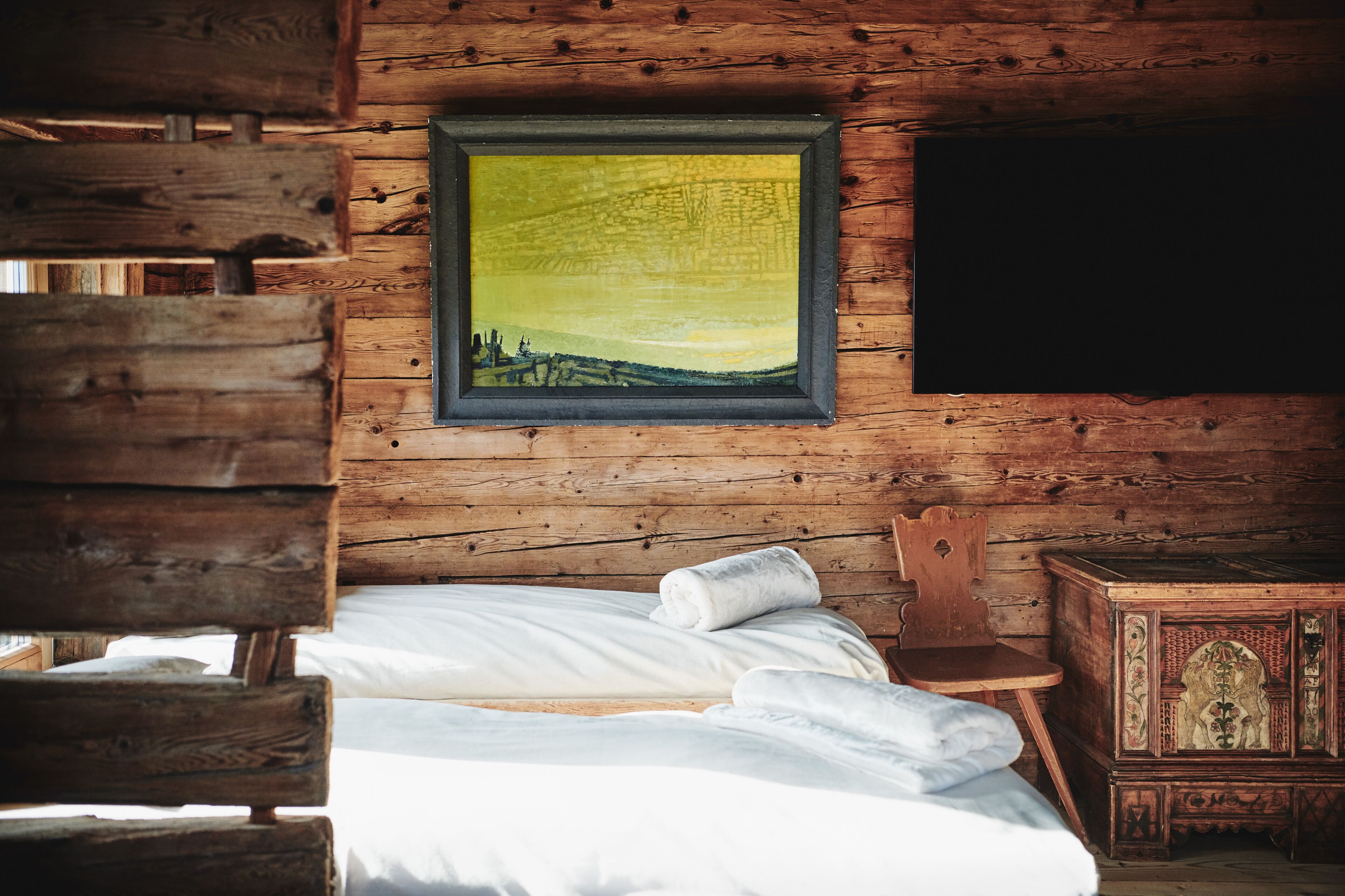 Una habitación de cabaña de madera con una cama, un sillón y un mueble pequeño.