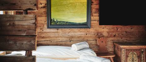 Una habitación de cabaña de madera con una cama, un sillón y un mueble pequeño.