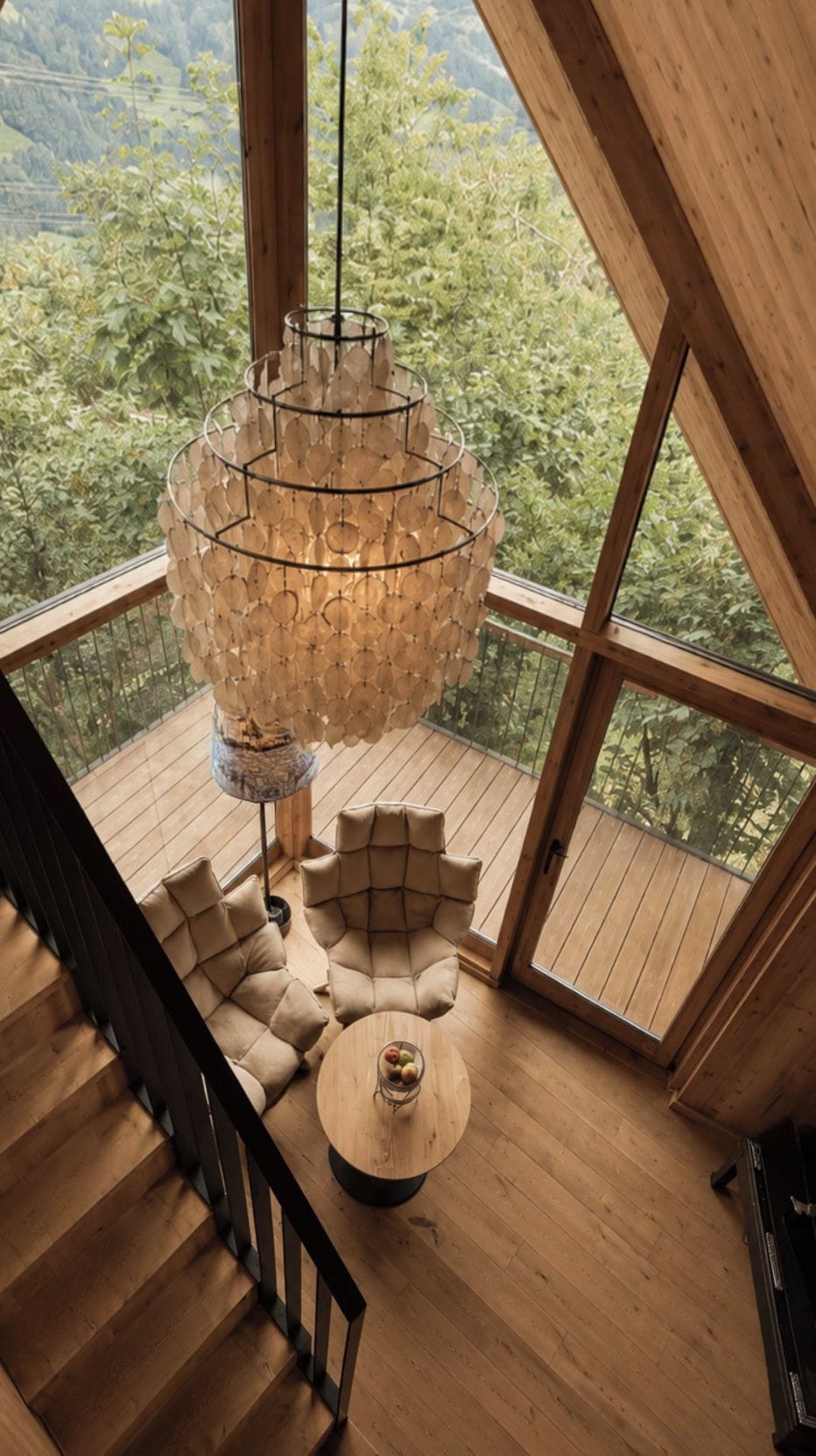 A wooden interior with a large window, a hanging light fixture, a sofa, and a round table.