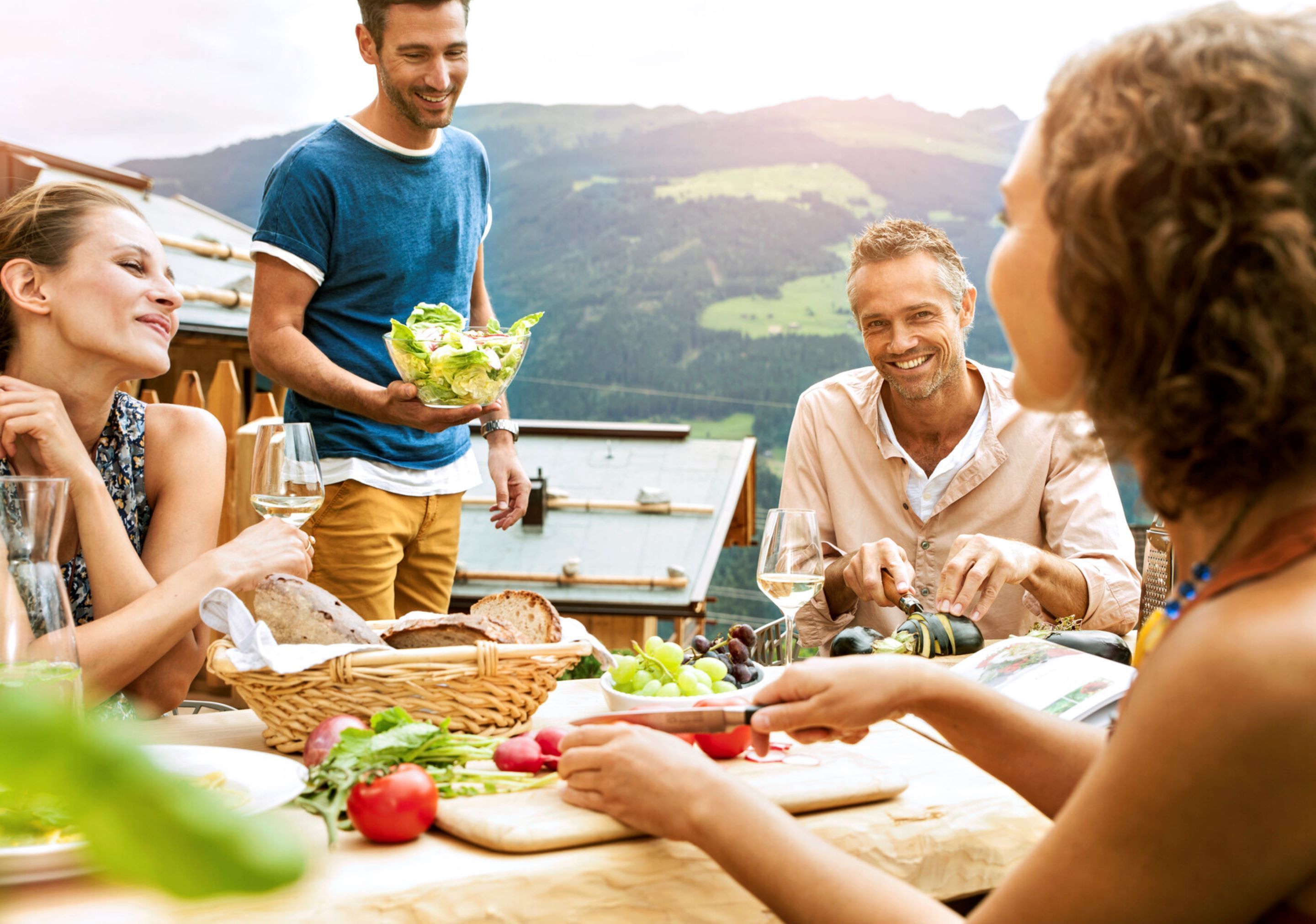 Un groupe de personnes est réuni autour d’une table en plein air, avec une vue panoramique sur les montagnes en arrière-plan.