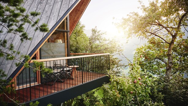 A wooden deck with a table and chairs, overlooking a forested area and a body of water.