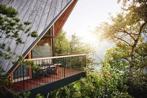 Um deck de madeira com mesa e cadeiras, com vista para uma área arborizada e um corpo d'água.